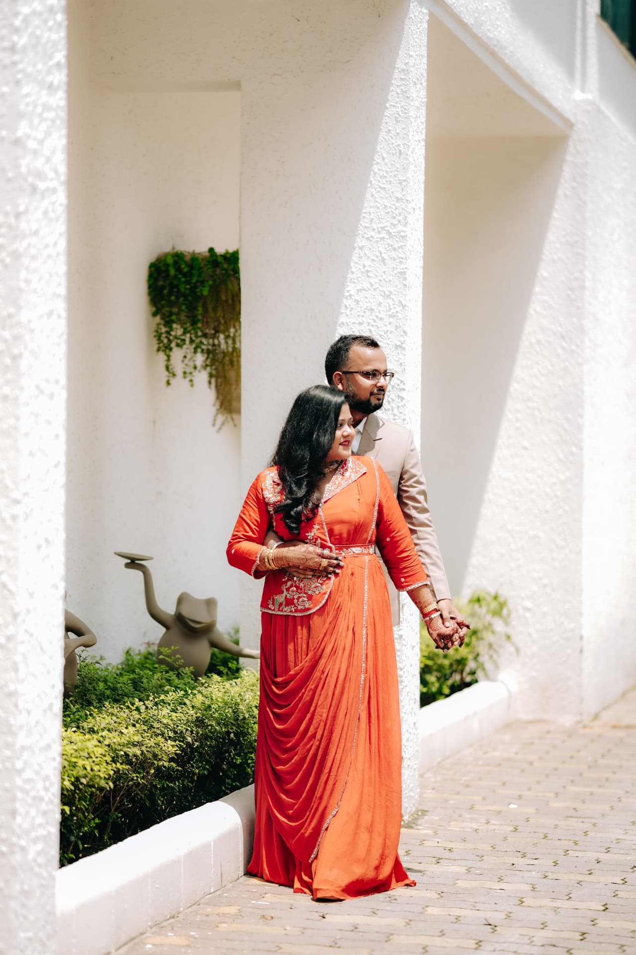 The couple standing together by a white wall
